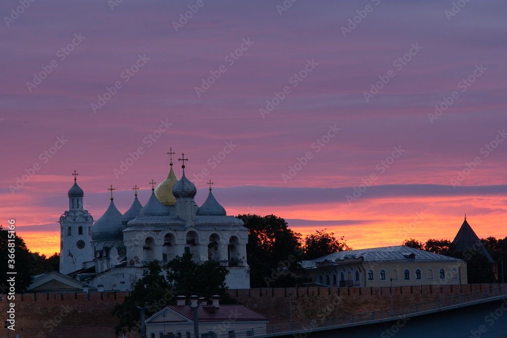Veliky Novgorod. The Novgorod Kremlin. Russia. The domes of the St. Sophia Cathedral, the belfry and the chapel against the orange sunset sky.