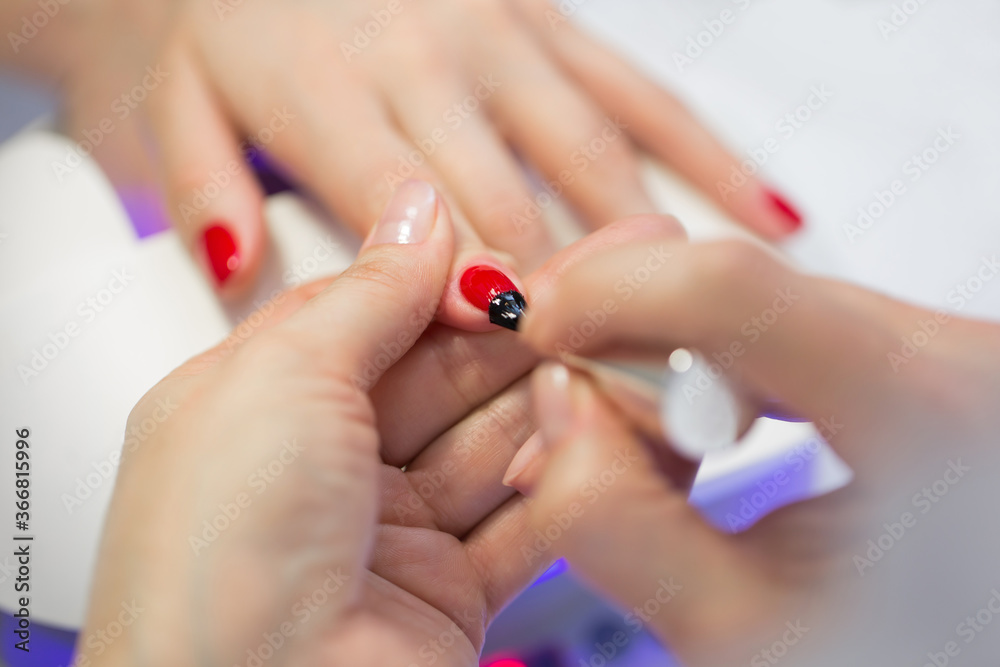 Naklejka premium Manicurist master makes red manicure on young woman hand. Woman nail master doing nails to a girl client at a beauty salon. Care for hands