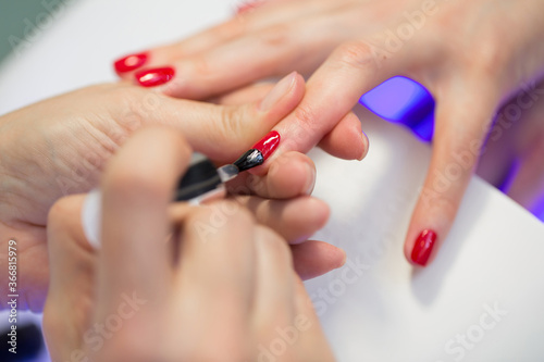 Manicurist master makes red manicure on young woman hand. Woman nail master doing nails to a girl client at a beauty salon. Care for hands