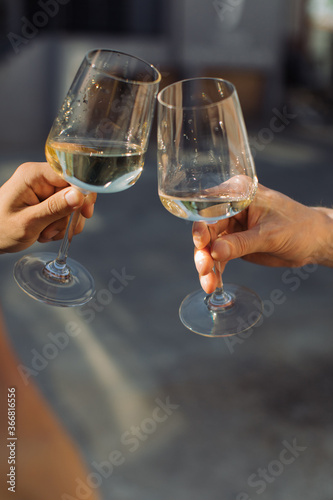 Friends making celebratory toast with glasses of white wine at summer party. Golden light, relax concept.