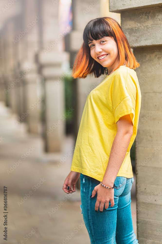 Fototapeta premium Alternative caucasian model with orange hair looking back smiling on a city background.