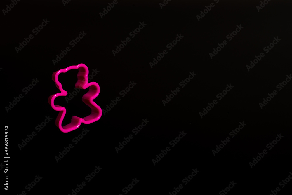 Pink plastic cookie cutter for making cookies in the shape of a teddy bear on a black background. Culinary concept. Flat lay with copyspace.