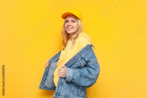 girl puts on a denim jacket on a yellow background and smiles