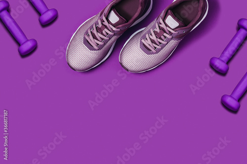 Purple background with sneakers and dumbbells. Flat lay picture.
