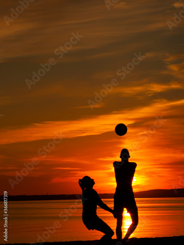Horizontal colourful picture with twoblack silhouettes of a man and a woman playing beach volleyball on the seashore in the evening against orange sunset