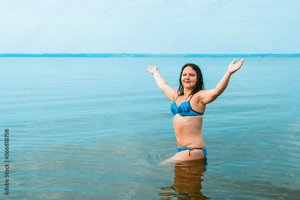 A brunette woman in a blue swimsuit at sunrise in the azure water near the shore.