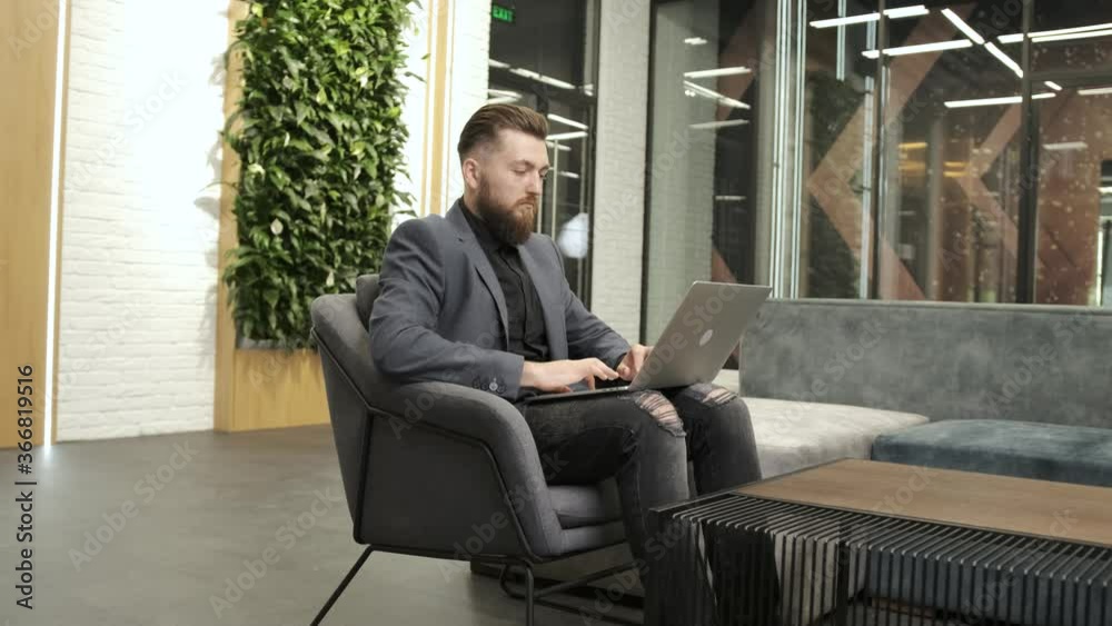 Bearded businessman working at the laptop in the business office. He is tired and exhausted after a long worker day Bearded businessman working at the laptop in the business office. He is tired and exhausted after a long worker day