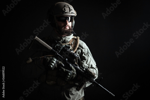 American commando in a military uniform with a weapon looks at copy space, a marine on a dark background, a member of the elite troops, war concept