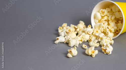 Popcorn in a yellow paper cup on grey background. Copy space