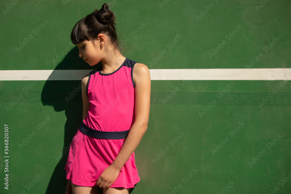 girl in a pink tennis dress posing on a tennis wall