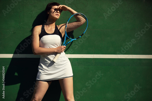 woman wearing white tennis dress posing on green tennis wall © kevin