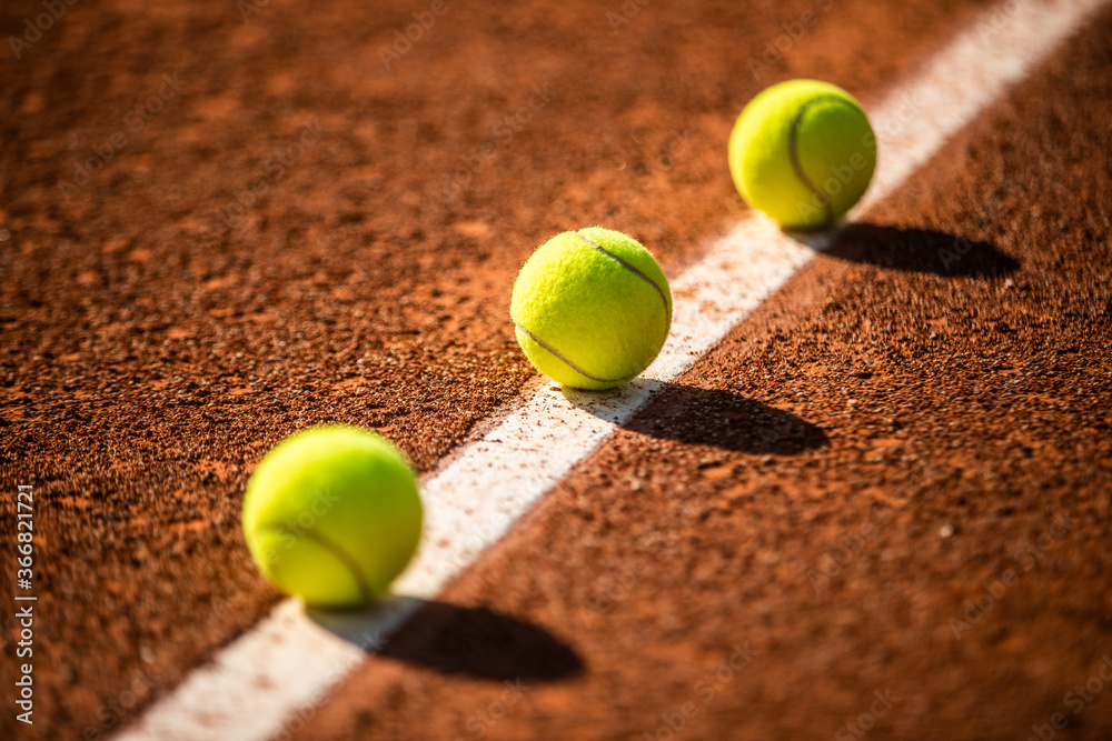 three tennis balls lined up on a white line of a clay tennis court