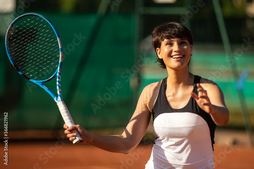 a smiling woman playing tennis outdoors on a clay court