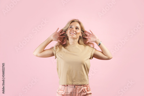 Gossip or rumors concept. Colorful portrait of amazed young woman with palms near her ears. Pink background
