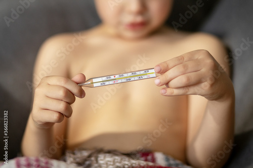 A close-up glass thermometer shows a temperature of thirty-seven degrees. The child's hands are holding a thermometer. Temperature measurement