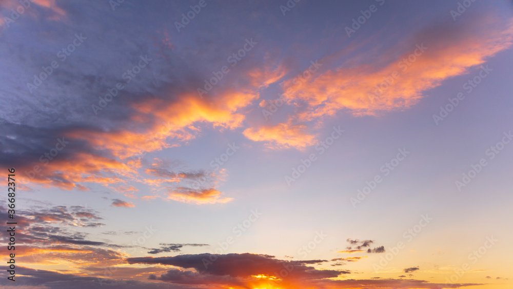 Idyllic and dramatic sunset sky with motion clouds in the English Warwickshire countryside. Purple, orange and golden tones. Background design asset.