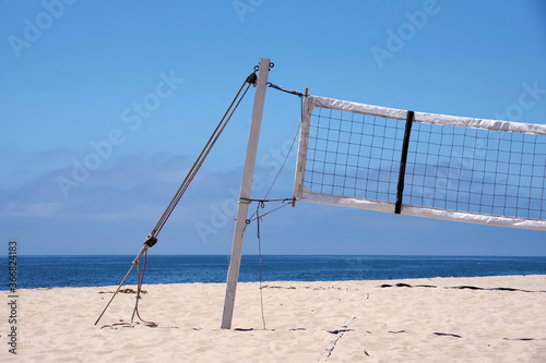 Partial view of a beach volleyball net at an empty beach in bright summer sunlight with blue sky and some fog clouds at the horizon over the ocean