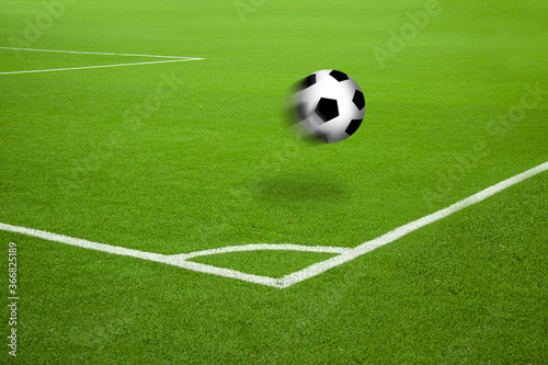 Football in motion on soccer court with white stripes corner markings. Saturated green grass and football in the air with motion blur and cast shadow.