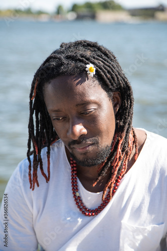 The guy of the African race, dreadlocks hairstyle, chamomile in his hair, sad against the background of the sea. photo
