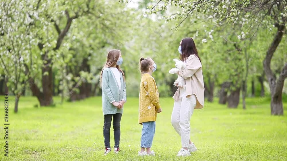 Family of mother and daughters in blooming cherry garden in masks Family of mother and daughters in blooming cherry garden in masks