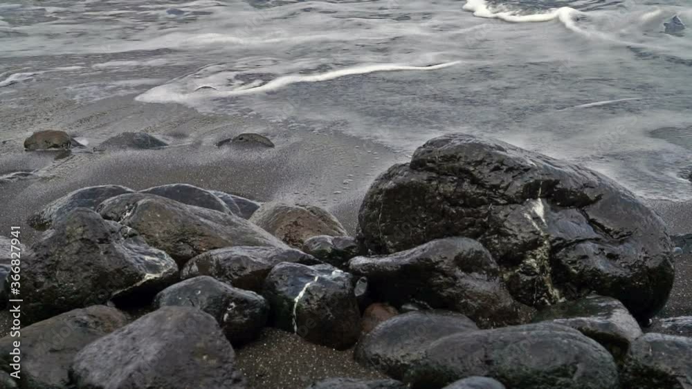 Sea waves run against black stones and dark sand. Sea waves run against black stones and dark sand.