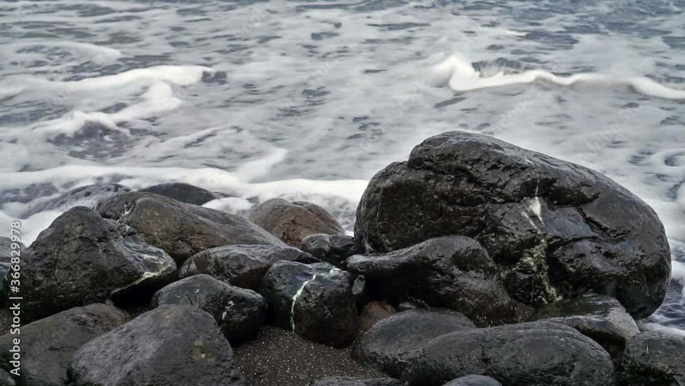Sea waves run against black stones and dark sand. Sea waves run against black stones and dark sand.