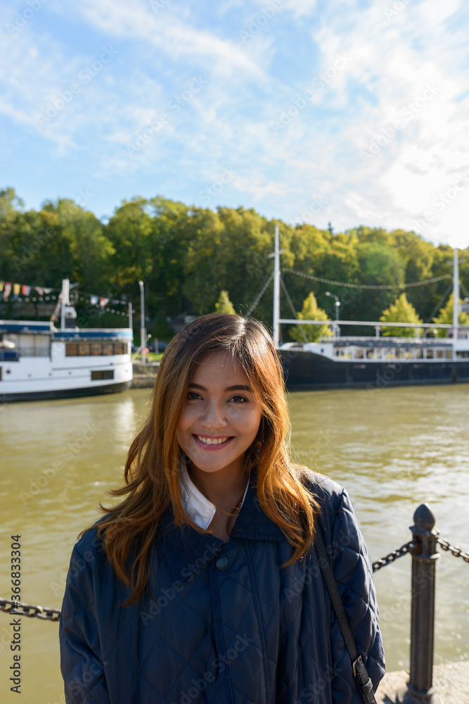 Young happy Asian woman standing in pier with vintage black boat in the river