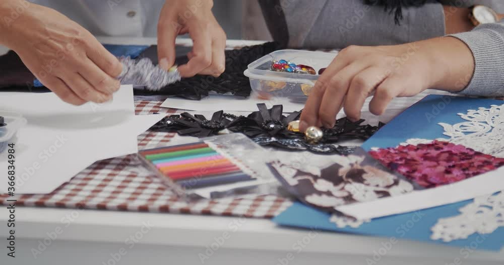 Close up of male and female designers sitting at table with sewing accessories and trying on different variants for new dress. Concept of teamwork and fashion business.