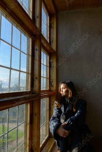 Young beautiful Asian woman sitting in front of closed wooden window with sunlight streaming in © Ranta Images