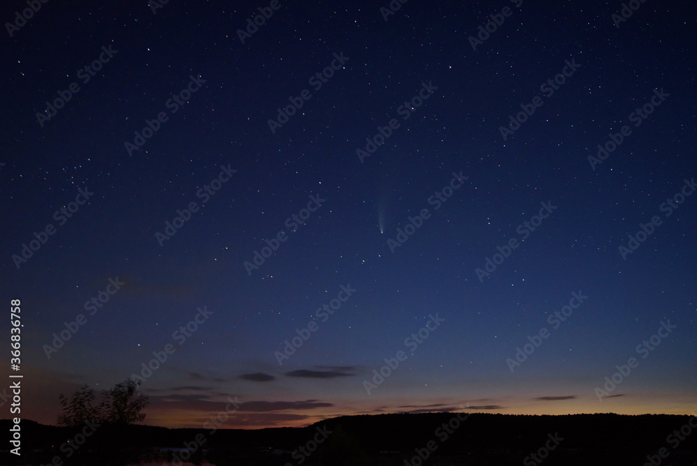 C / 2020 F3 comet (NEOWISE) at sunset. Landscape with wheat field and bales on horizon with a tree silhouette. At night, there is a bright comet and tail among the stars. Photographed in Hungary C / 2020 F3 comet (NEOWISE) at sunset. Landscape with wheat field and bales on horizon with a tree silhouette. At night, there is a bright comet and tail among the stars. Photographed in Hungary