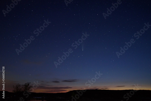 C   2020 F3 comet  NEOWISE  at sunset. Landscape with wheat field and bales on horizon with a tree silhouette. At night  there is a bright comet and tail among the stars. Photographed in Hungary