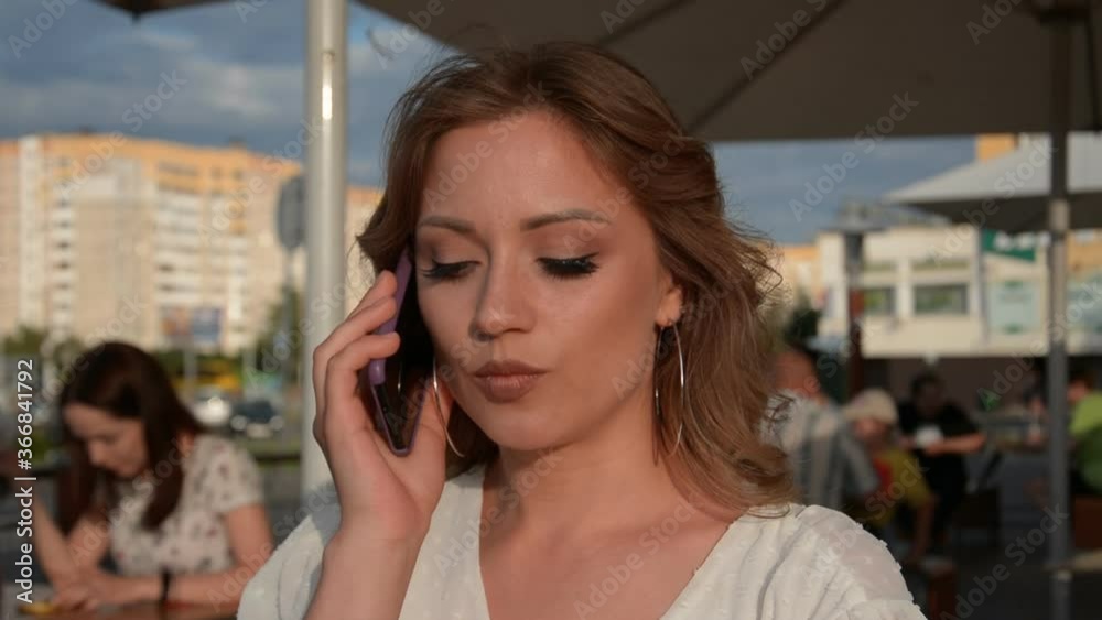 stylish girl portrait sitting in a restaurant in the evening in the summer and talking on a cell phone with her friend stylish girl portrait sitting in a restaurant in the evening in the summer and talking on a cell phone with her friend