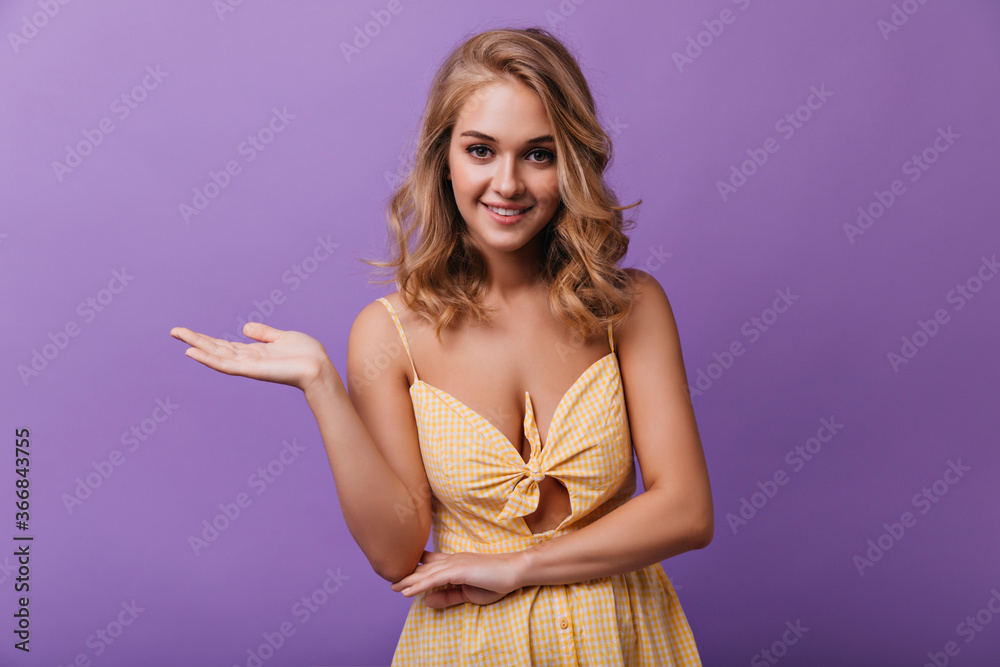 Obraz premium Graceful carefree girl smiling on purple background. Studio photo of gorgeous curly woman in yellow dress.