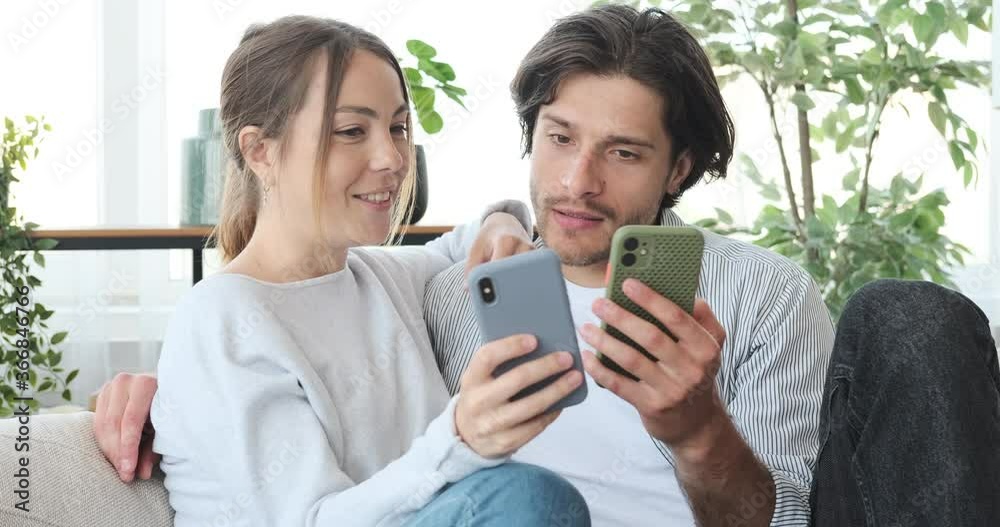 Couple discussing and using mobile phone on sofa at home Couple discussing and using mobile phone on sofa at home