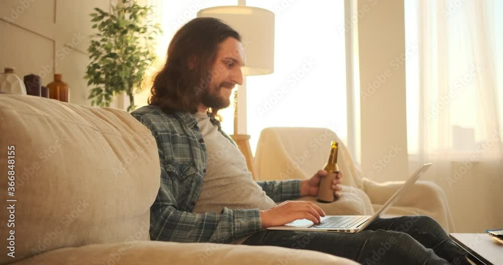 Handsome man using laptop and drinking beer at home