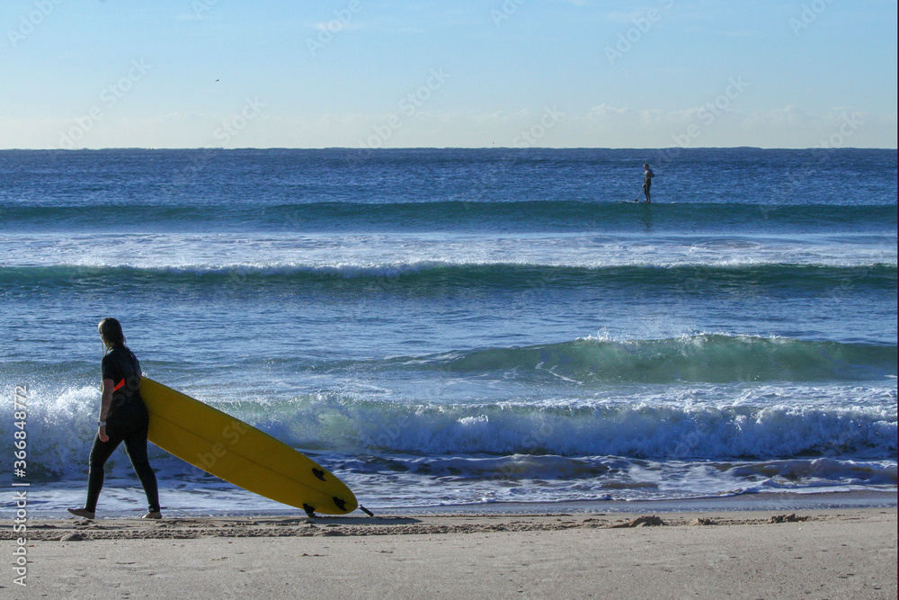 Girl surfer walking along beach with yellow surfboard with ocean in background
Girl surfer walking along beach with yellow surfboard with ocean in background