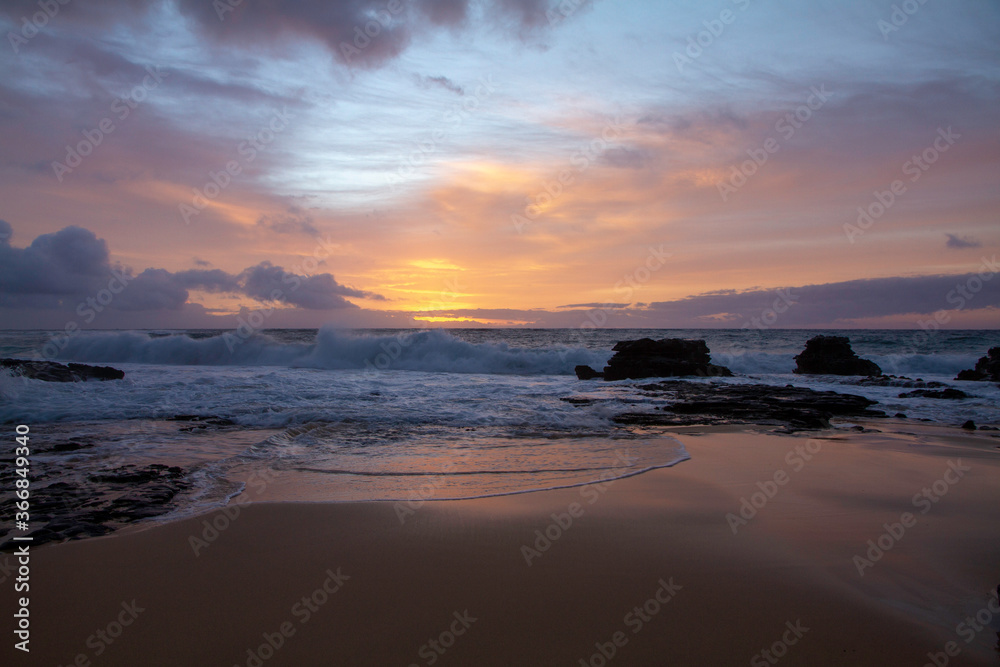 orange and purple sunrise in Hawaii, with the sunrise reflecting into the water on the sand