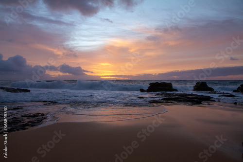 orange and purple sunrise in Hawaii, with the sunrise reflecting into the water on the sand