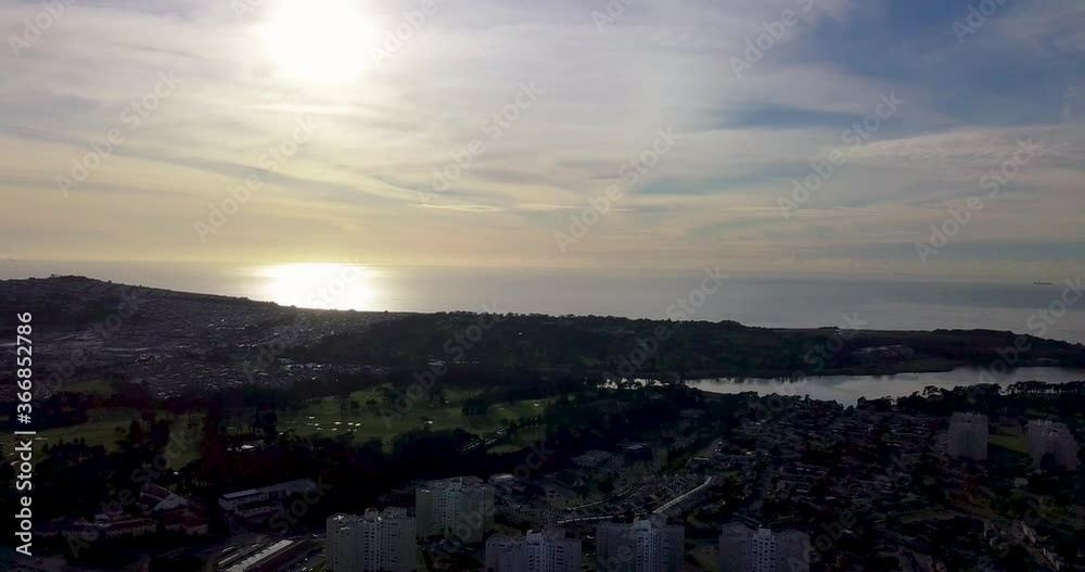 Sunset ocean over a Golf course fly up and down loop to Ocean waves reflecting sun under blue sky clouds green grass trees and hazy horizon Sunset ocean over a Golf course fly up and down loop to Ocean waves reflecting sun under blue sky clouds green grass trees and hazy horizon