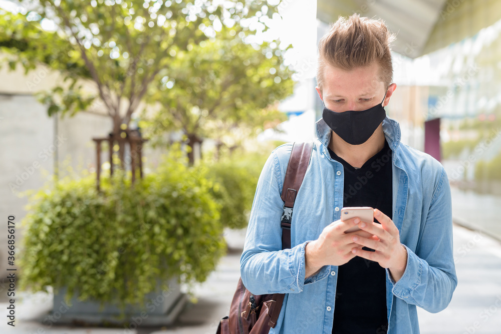 Fototapeta premium Portrait of man with mask using phone in the city streets outdoors