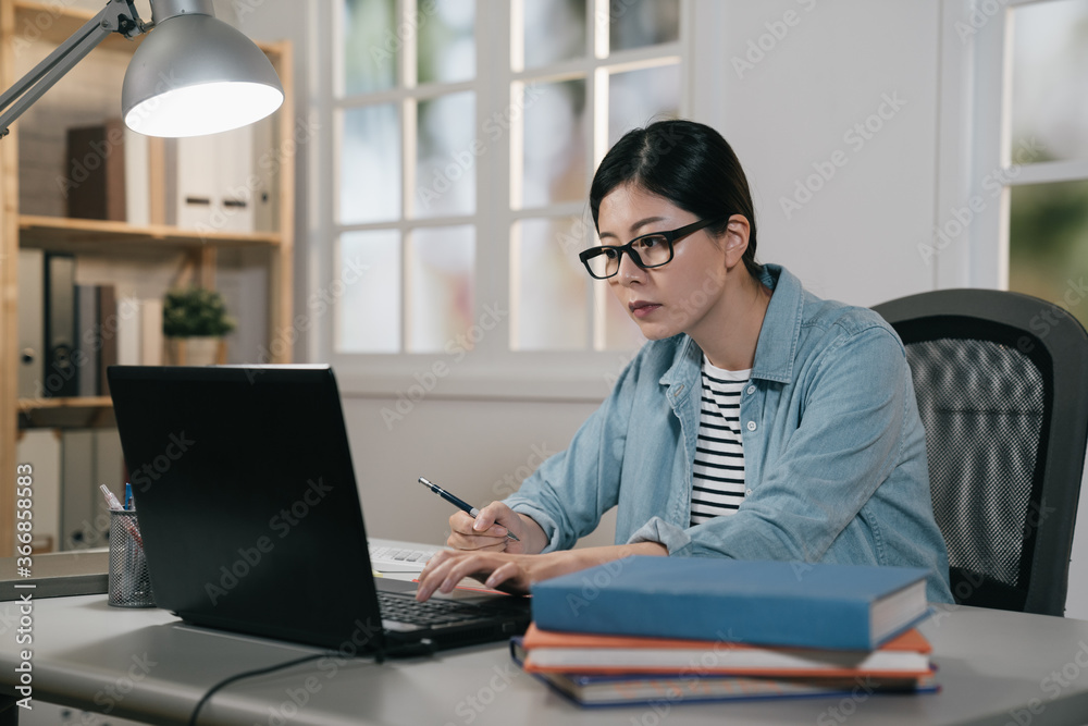 Young attractive female student scribing notes to textbook prepare for exam. college girl doing homework sitting with modern laptop computer. asian chinese woman in glasses making plan for test Young attractive female student scribing notes to textbook prepare for exam. college girl doing homework sitting with modern laptop computer. asian chinese woman in glasses making plan for test