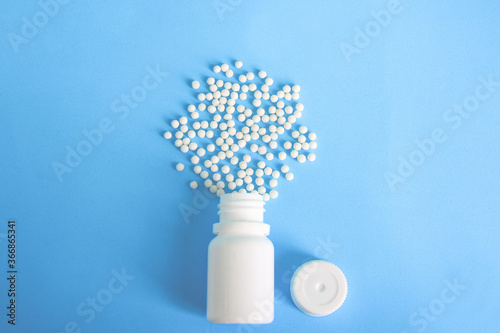 Homeopathic pills, globules and white plastic bottle on blue background. Alternative Homeopathy medicine herbs, healtcare and pills concept. Flatlay. Top view. 