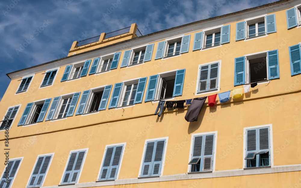 Traditional colorful painted building facade with blue shutters and laundry hanging in Bastia, Corsica, France