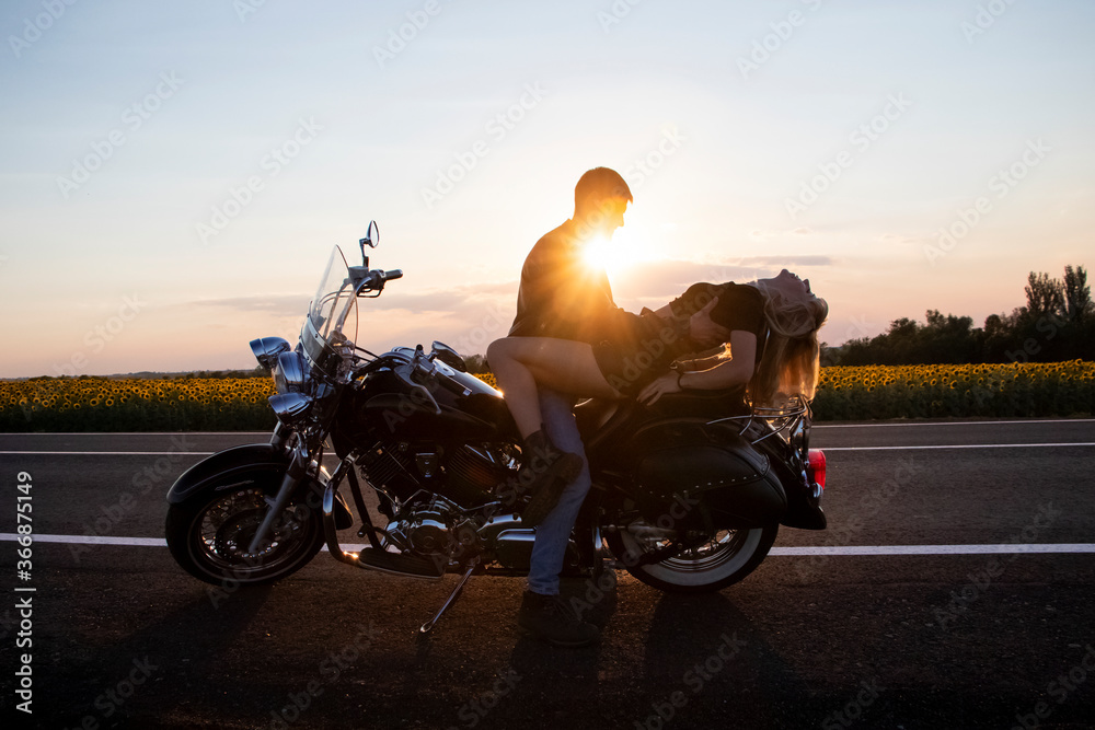 Bikers man and woman stopped at the side of the road to rest and kiss passionately. Photos of loving motorcyclists at sunset. The concept of freedom, brutality and passion