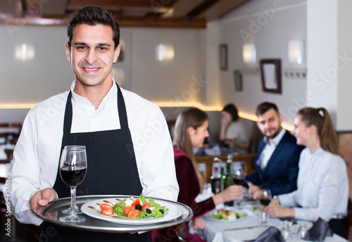 cheerful waiter with serving tray welcoming to cozy restaurant