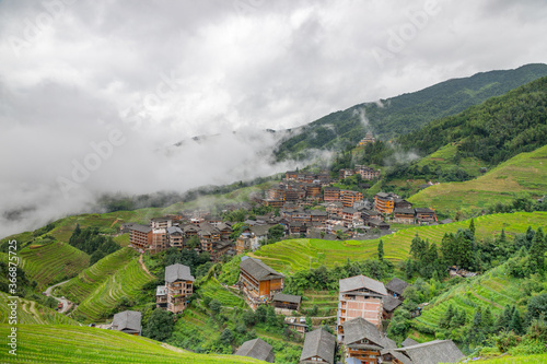 picturesque paddy rice terraces and village houses in Jinkeng, Longji, Guangxi, China in a foggy and cloudy day with occasional rainfall photo