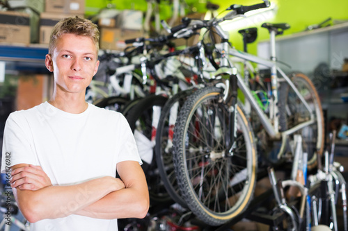 Portrait of young attractive male standing near the cycle in the shop
