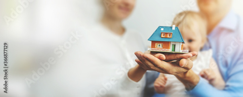new family home concept - young parents and child with dream house scale model in hands. copy space