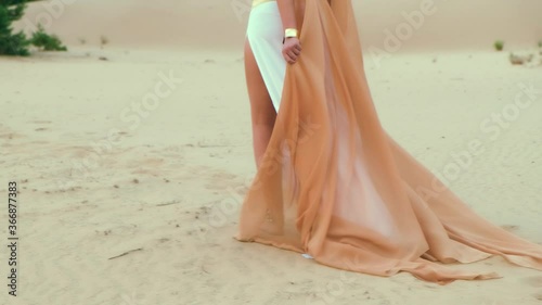 Closeup portrait beautiful female legs walking, hot summer beach, Egyptian desert. Beauty bare feet. Gold jewelry for legs profiles, payals, bracelets. White long dress, orange cloak. Trees, pyramids photo