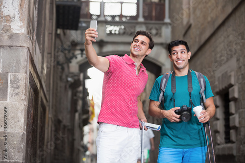 Men are walking with baggage and making selfie near sights in Barcelona